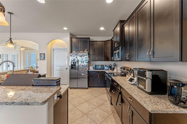 kitchen featuring appliances with stainless steel finishes, light stone counters, dark brown cabinets, a textured ceiling, and hanging light fixtures