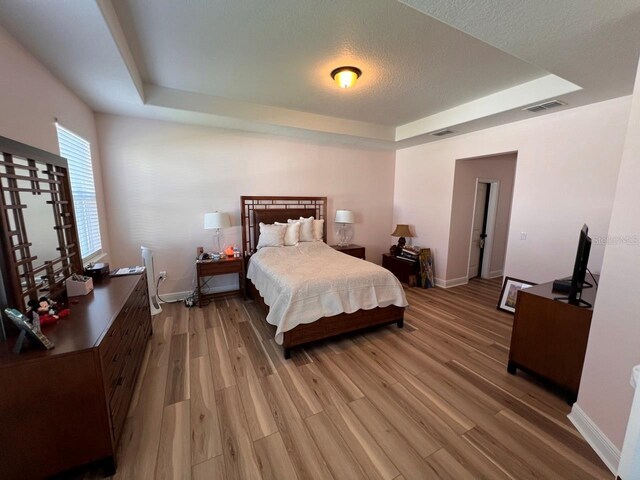 bedroom featuring hardwood / wood-style flooring, a tray ceiling, and a textured ceiling