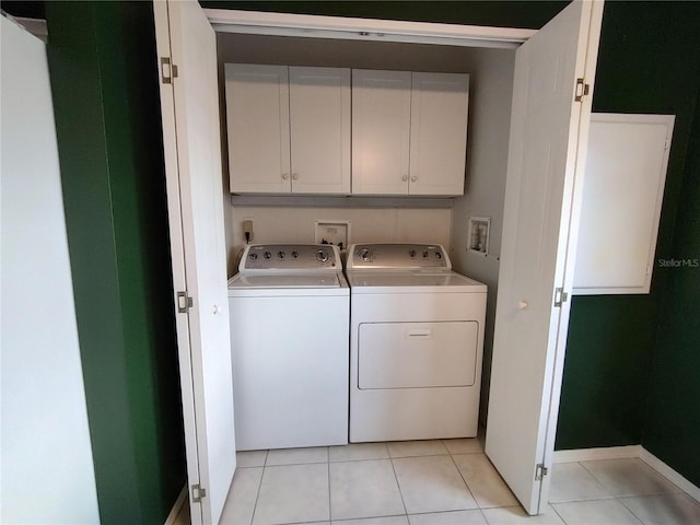 clothes washing area featuring cabinets, light tile patterned floors, and washing machine and clothes dryer