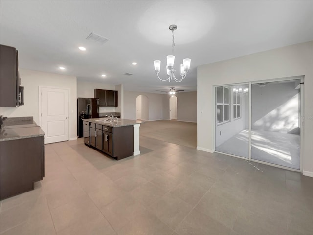 kitchen with pendant lighting, black fridge, an island with sink, dark brown cabinets, and light stone counters