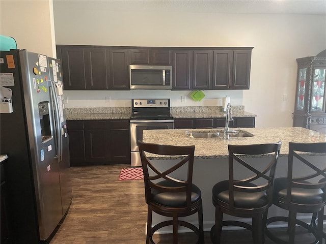 kitchen featuring sink, dark wood-type flooring, stainless steel appliances, light stone counters, and a breakfast bar area