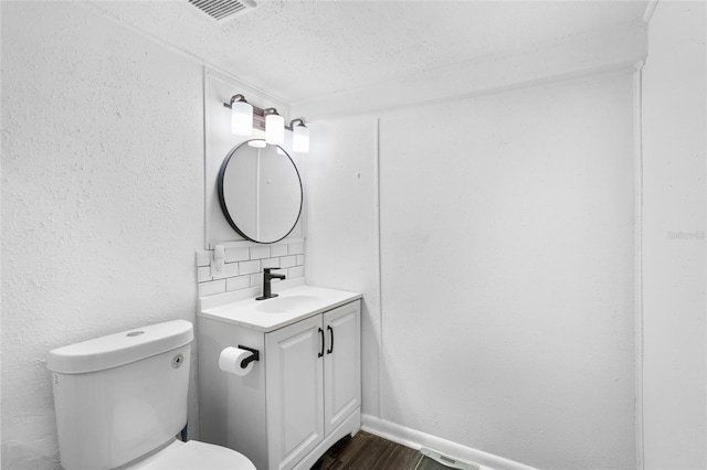 bathroom with backsplash, vanity, a textured ceiling, hardwood / wood-style floors, and toilet