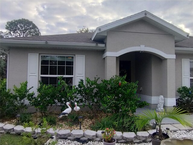 entrance to property with stucco siding and roof with shingles