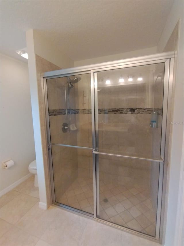 bathroom featuring tile patterned floors, baseboards, toilet, and a stall shower