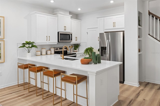 kitchen featuring kitchen peninsula, appliances with stainless steel finishes, white cabinetry, and a breakfast bar area