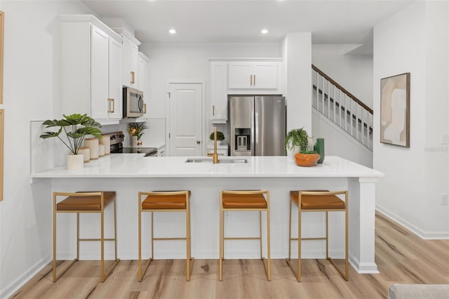 kitchen with kitchen peninsula, appliances with stainless steel finishes, light hardwood / wood-style flooring, and a kitchen breakfast bar