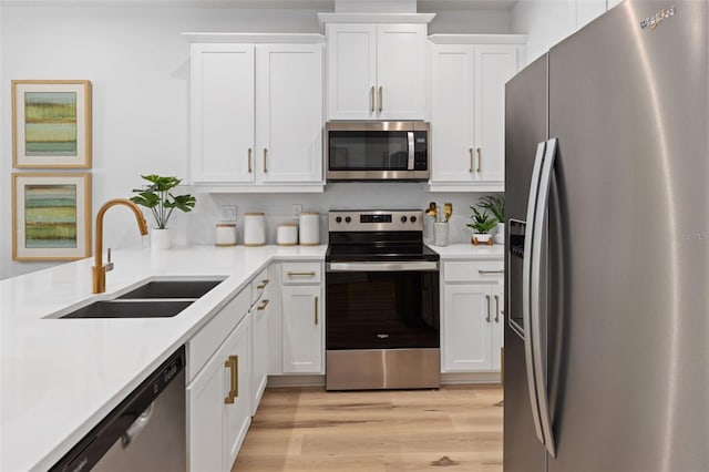 kitchen with appliances with stainless steel finishes, light wood-type flooring, white cabinetry, and sink