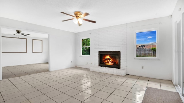 unfurnished living room with ceiling fan, a fireplace, light tile patterned floors, and a healthy amount of sunlight