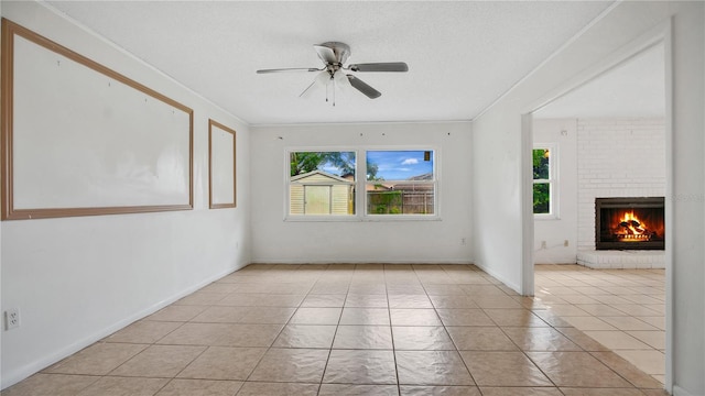 tiled empty room with a textured ceiling, ceiling fan, crown molding, and a fireplace