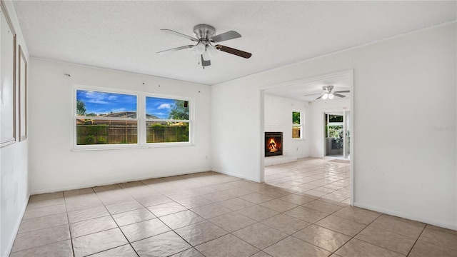 tiled spare room featuring ceiling fan, ornamental molding, a textured ceiling, and a brick fireplace