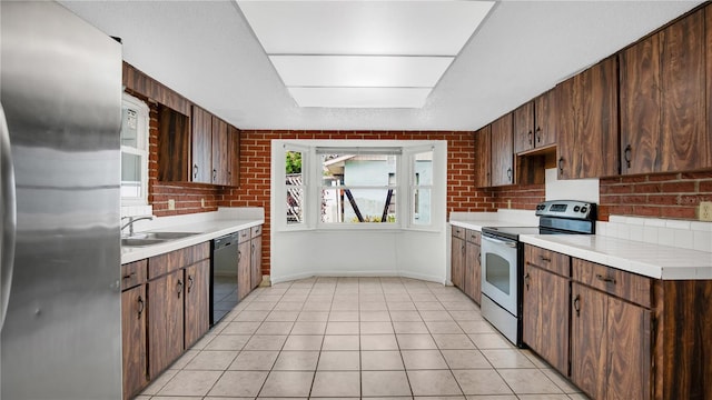 kitchen featuring brick wall, dark brown cabinetry, stainless steel appliances, and light tile patterned floors