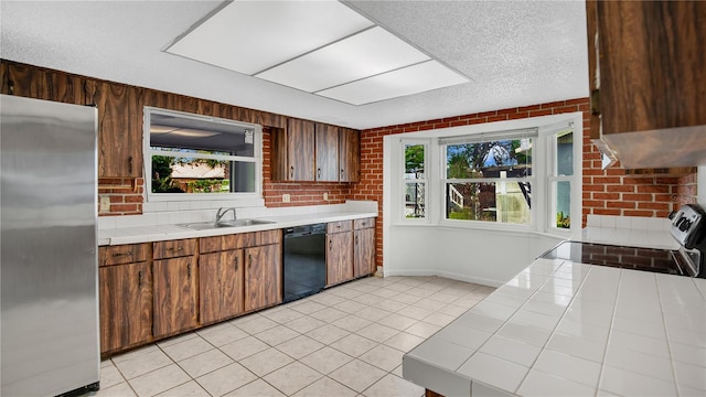 kitchen with a textured ceiling, tile countertops, stainless steel appliances, and brick wall