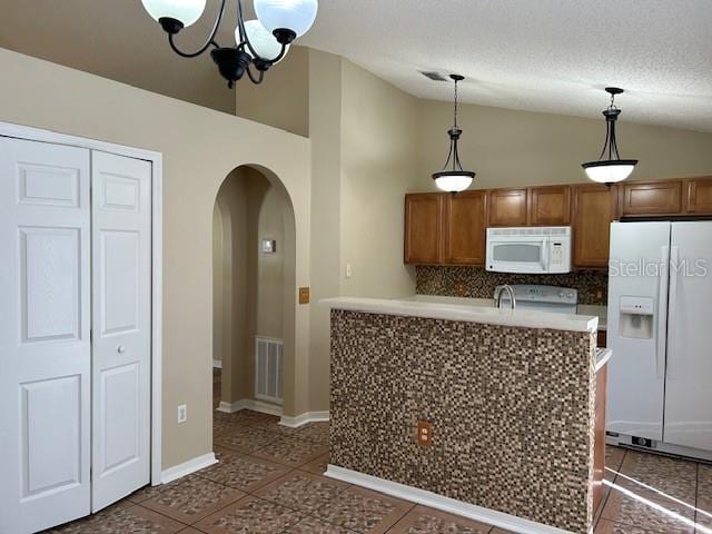 kitchen with dark tile patterned flooring, white appliances, hanging light fixtures, and vaulted ceiling