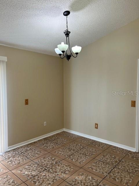 tiled empty room featuring a chandelier and a textured ceiling