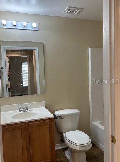 full bathroom featuring washtub / shower combination, wood-type flooring, vanity, and toilet