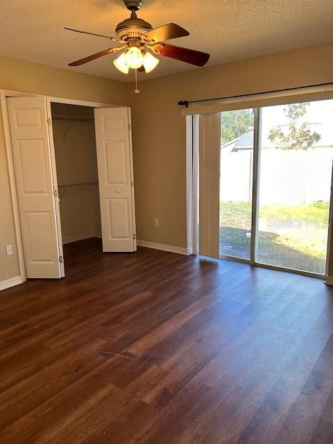 unfurnished bedroom featuring a closet, access to outside, ceiling fan, and dark wood-type flooring