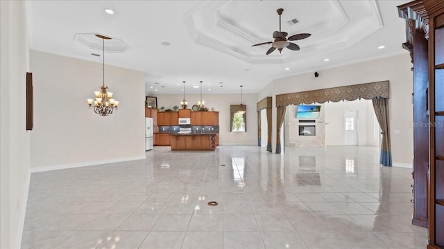 unfurnished living room with ceiling fan with notable chandelier, a tray ceiling, and ornamental molding