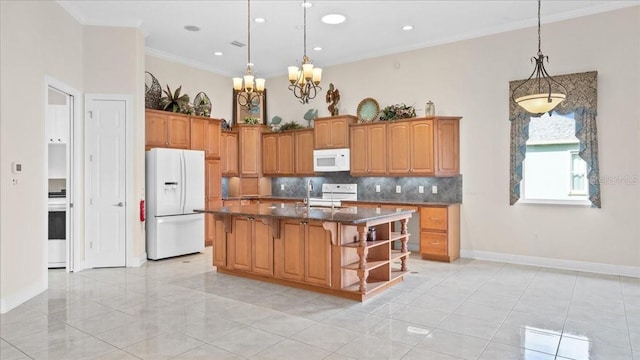 kitchen featuring decorative backsplash, crown molding, pendant lighting, white appliances, and a kitchen island with sink