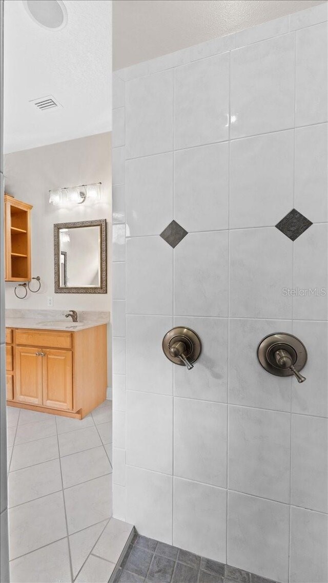 bathroom with a tile shower, vanity, and tile patterned floors