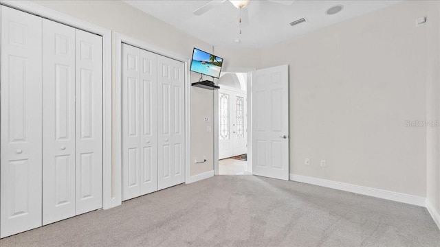 unfurnished bedroom featuring ceiling fan, light carpet, and two closets