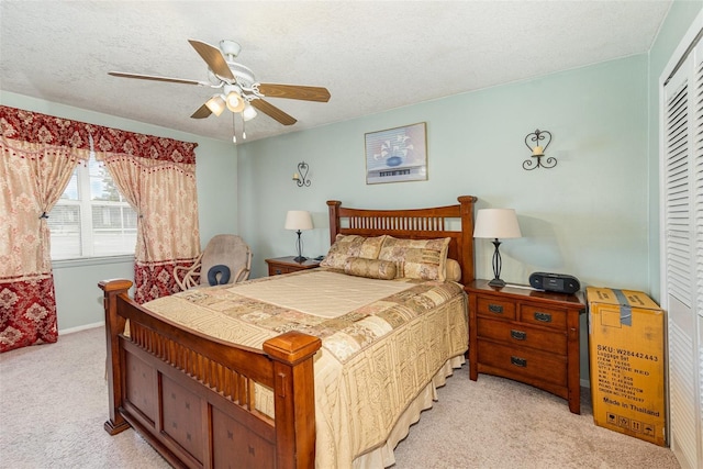 bedroom with a textured ceiling, a closet, light colored carpet, and ceiling fan