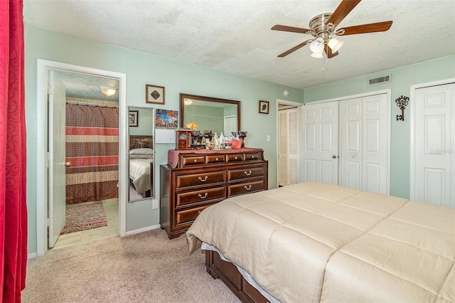 bedroom featuring multiple closets, ceiling fan, light colored carpet, and a textured ceiling