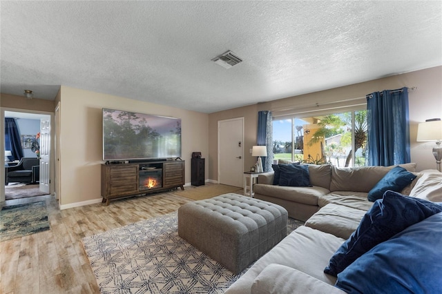 living room with a fireplace, a textured ceiling, and light hardwood / wood-style flooring