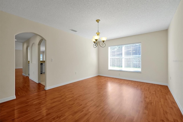 spare room with hardwood / wood-style floors, a textured ceiling, and a notable chandelier