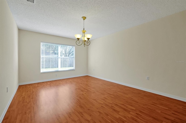 empty room with a notable chandelier, wood-type flooring, and a textured ceiling