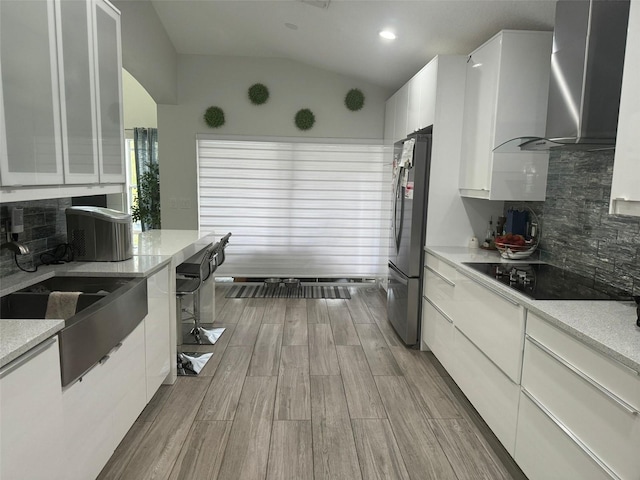 kitchen with white cabinetry, wall chimney exhaust hood, light hardwood / wood-style flooring, lofted ceiling, and decorative backsplash