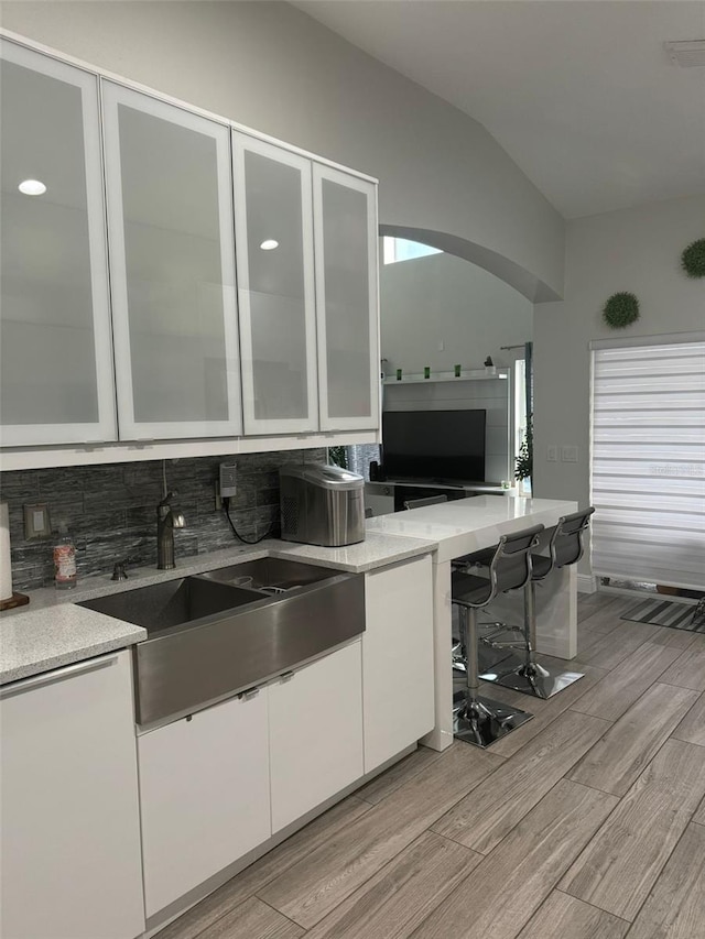 kitchen featuring decorative backsplash, light wood-type flooring, vaulted ceiling, sink, and white cabinetry