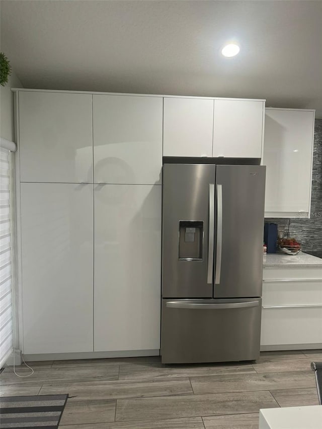 kitchen with white cabinets, decorative backsplash, stainless steel fridge, and light hardwood / wood-style flooring