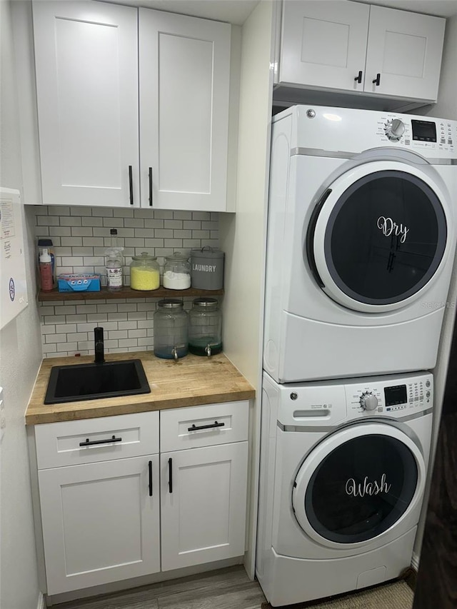 clothes washing area with cabinets, stacked washer and dryer, light hardwood / wood-style floors, and sink