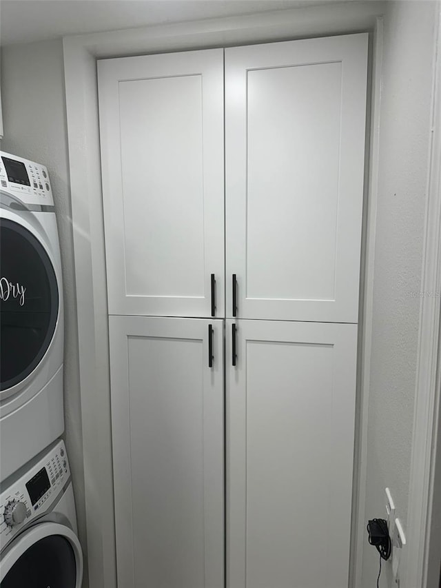 laundry area with cabinets and stacked washer and clothes dryer