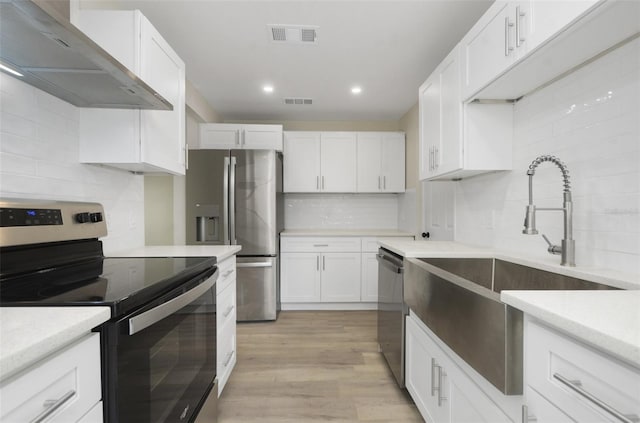 kitchen featuring white cabinetry, wall chimney exhaust hood, backsplash, light hardwood / wood-style floors, and appliances with stainless steel finishes