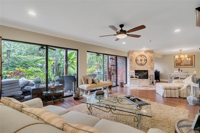 living room featuring a premium fireplace, wood-type flooring, ceiling fan with notable chandelier, and ornamental molding