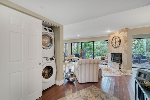 clothes washing area with a large fireplace, dark hardwood / wood-style floors, stacked washer / dryer, and ornamental molding