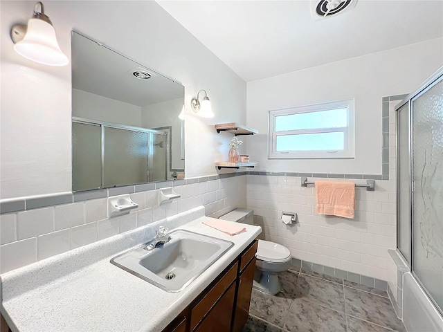 full bathroom featuring tile walls, shower / bath combination with glass door, tile patterned flooring, vanity, and toilet