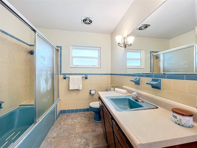 full bathroom featuring a healthy amount of sunlight, toilet, tile walls, and vanity