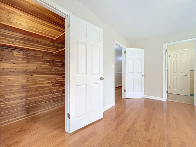 unfurnished bedroom featuring a walk in closet, light wood-type flooring, and wood walls