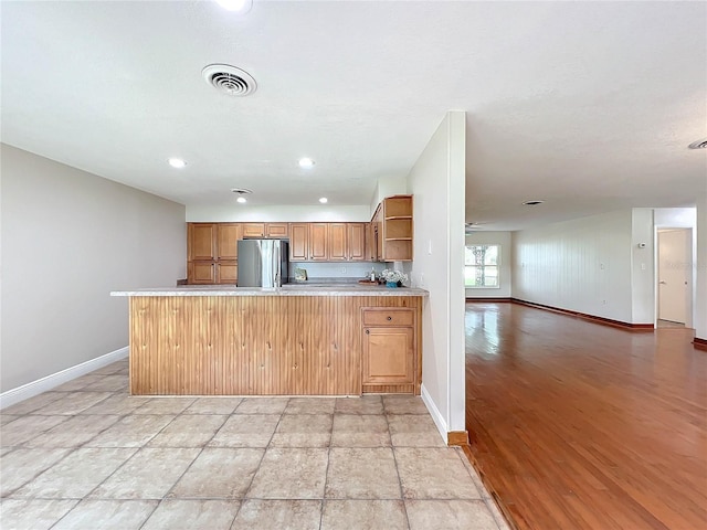 kitchen with visible vents, stainless steel refrigerator, open floor plan, a peninsula, and open shelves