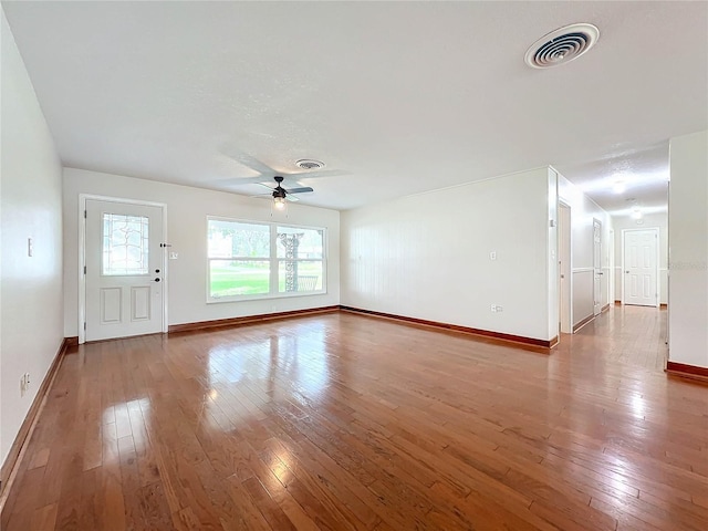 unfurnished living room with ceiling fan, hardwood / wood-style floors, visible vents, and baseboards