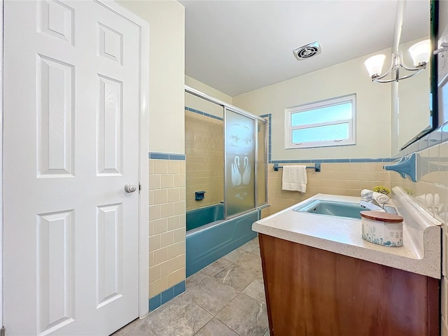 full bath with visible vents, wainscoting, combined bath / shower with glass door, vanity, and tile walls