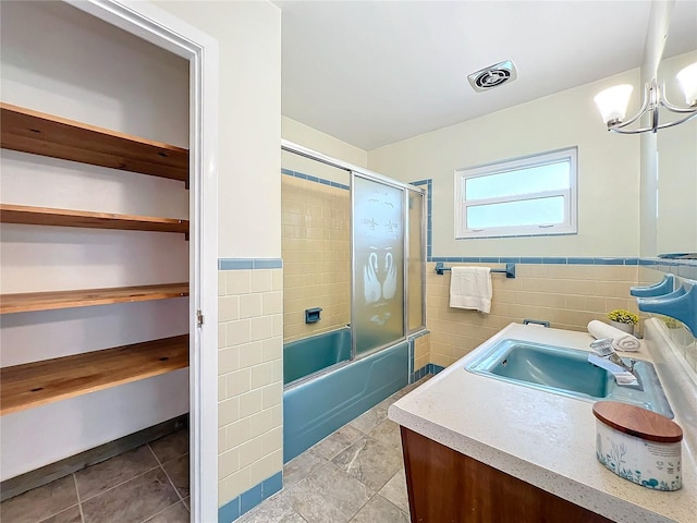 bathroom featuring visible vents, shower / bath combination with glass door, a wainscoted wall, vanity, and tile walls