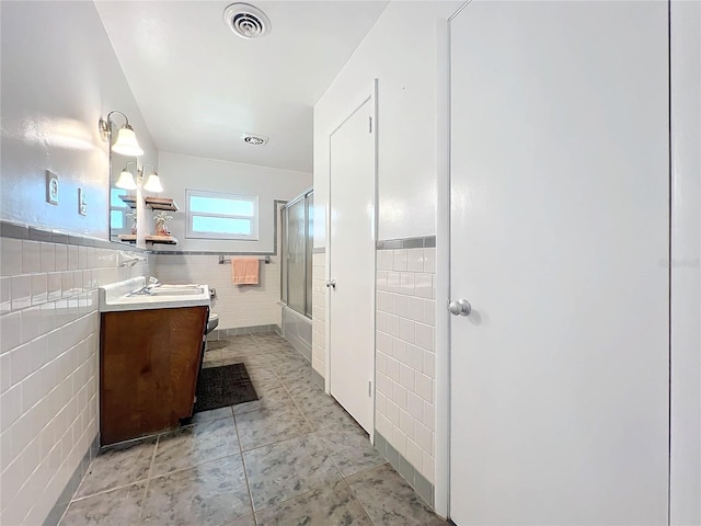 bathroom with visible vents, bath / shower combo with glass door, tile patterned floors, vanity, and tile walls