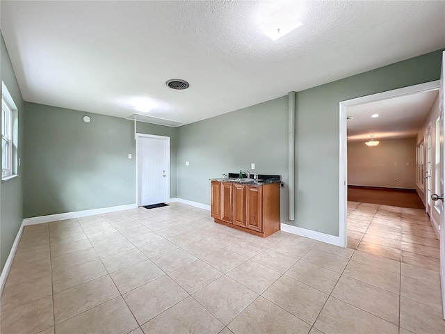 unfurnished room featuring a textured ceiling, light tile patterned flooring, a sink, visible vents, and baseboards