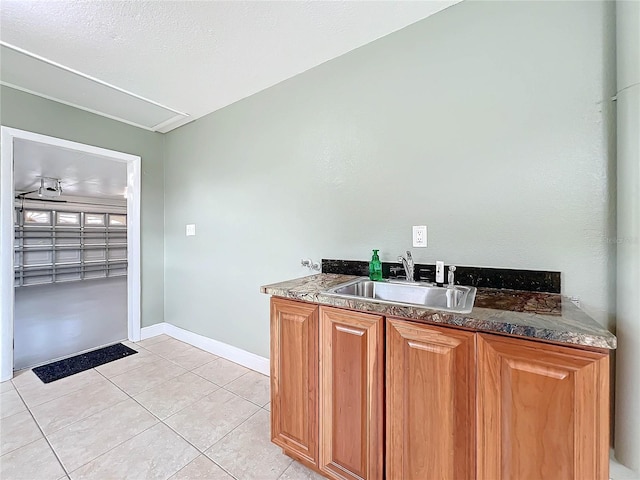 kitchen featuring light tile patterned floors, baseboards, dark stone counters, brown cabinetry, and a sink