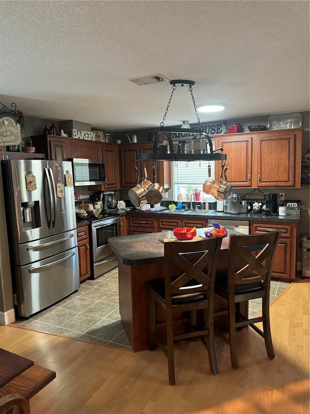 kitchen featuring pendant lighting, a textured ceiling, stainless steel appliances, and light hardwood / wood-style flooring