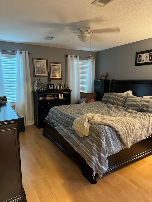 bedroom featuring multiple windows, ceiling fan, light hardwood / wood-style floors, and a textured ceiling