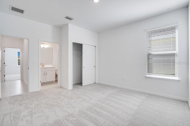 unfurnished bedroom featuring ensuite bathroom, a closet, and light colored carpet